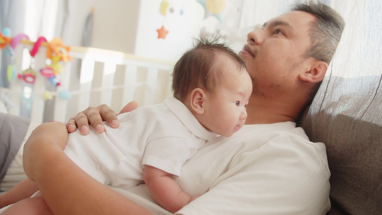 幸福亚洲父亲享受休息时间一起关心拥抱可爱的新生女婴躺在床上早上在家里，父亲爱的关系概念视频下载