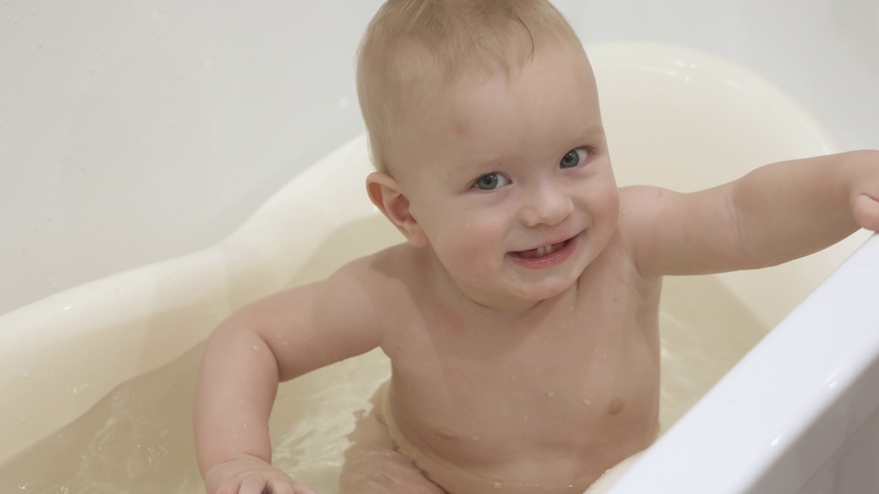 可爱的小孩在洗澡和玩玩具，小孩在玩洗澡玩具橡皮球，10个月大的婴儿在清洁的水洗澡的特写。儿童卫生和保健概念视频购买