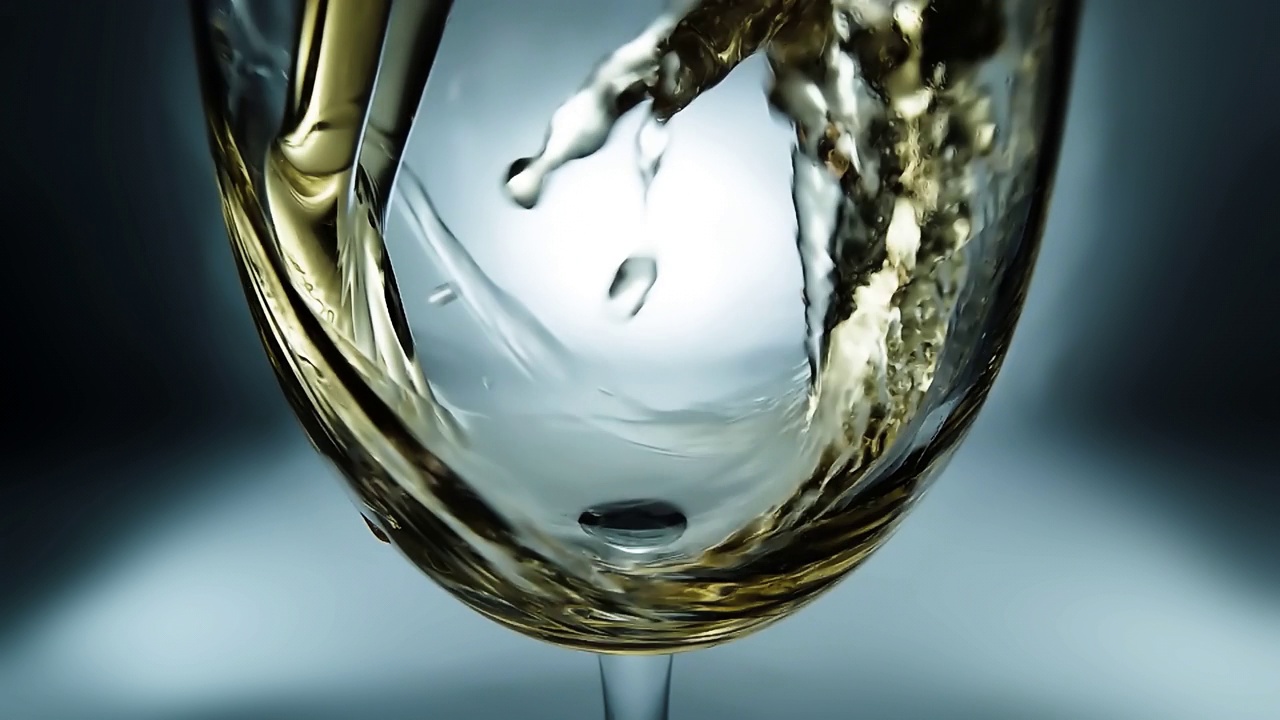 创意的4k微距慢动作视频白葡萄酒倒入杯子。酒杯与倒白葡萄酒的特写与飞溅和气泡。视频下载