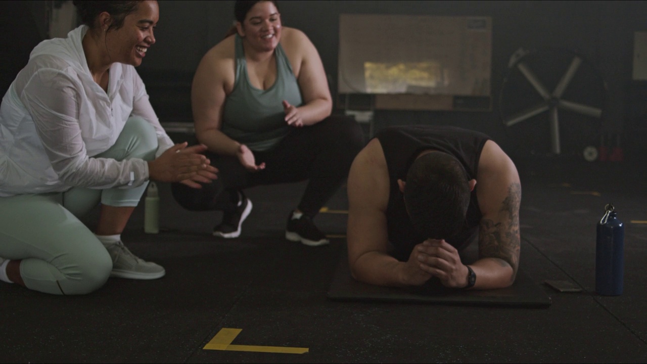 在一段4k视频中，一名男子在健身房保持平板支撑姿势，其他人在为他加油视频素材