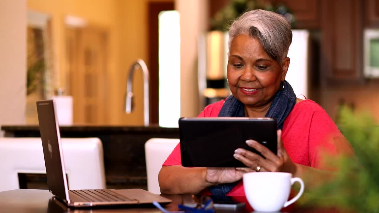 老年女性在家使用数码平板电脑和笔记本电脑。视频下载