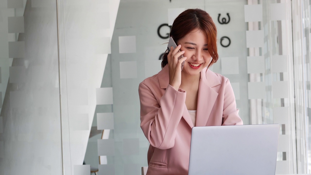 年轻的商业亚洲妇女专业的电话使用笔记本电脑坐在书桌前。视频素材