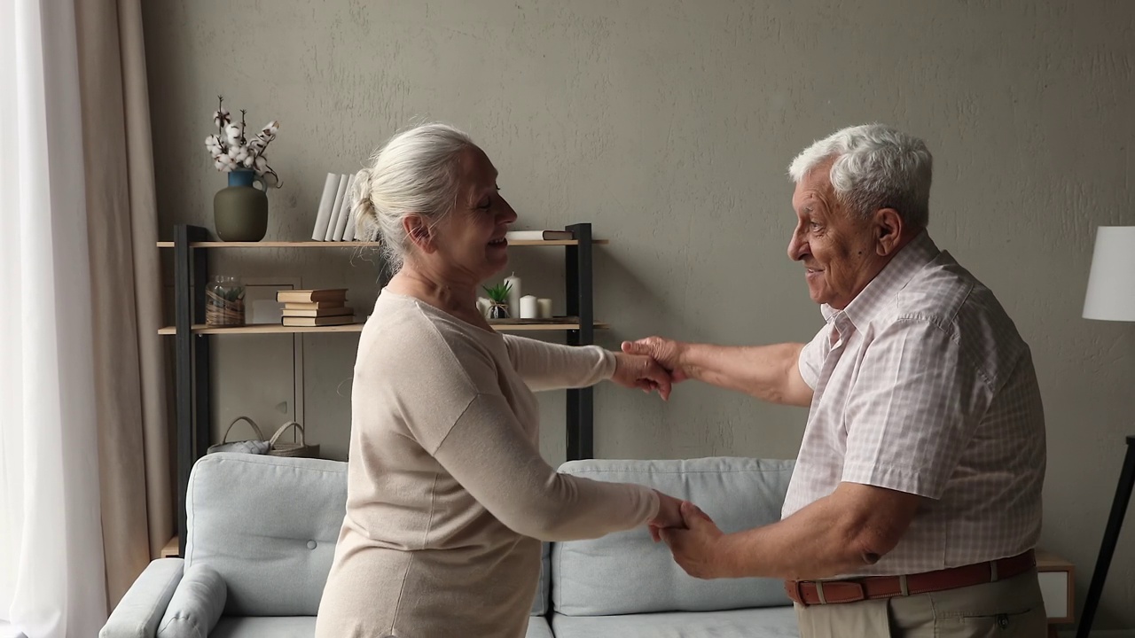 无忧无虑健康的退休配偶在客厅里手拉手跳舞视频下载