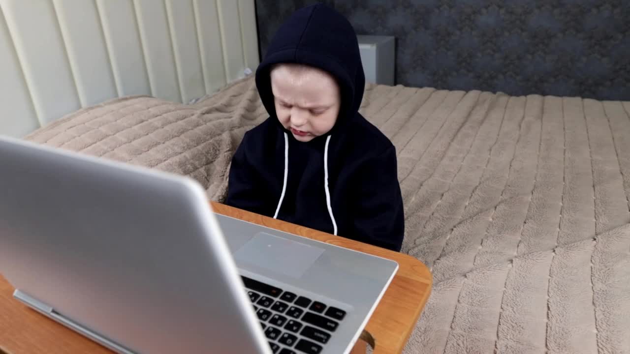 一个学龄前的男孩坐在卧室里的笔记本电脑前视频素材