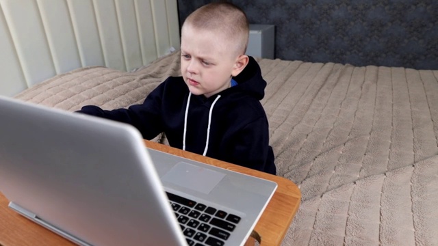 一个学龄前的男孩坐在卧室里的笔记本电脑前视频下载