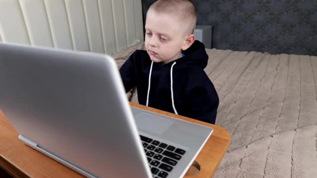 一个小男孩坐在一张大床上的笔记本电脑前，穿上他的运动衫兜帽视频素材