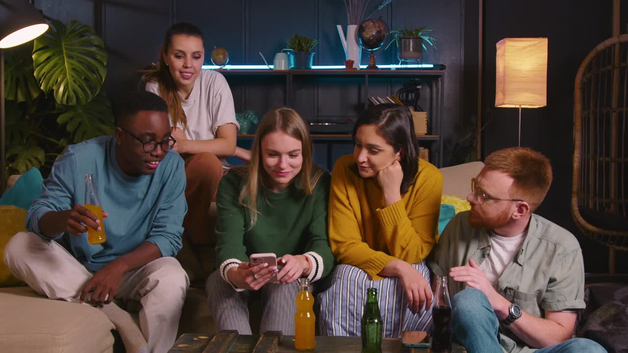 快乐的乐趣微笑的多民族年轻学生朋友享受饮料庆祝节日一起放松在家里的沙发上视频素材