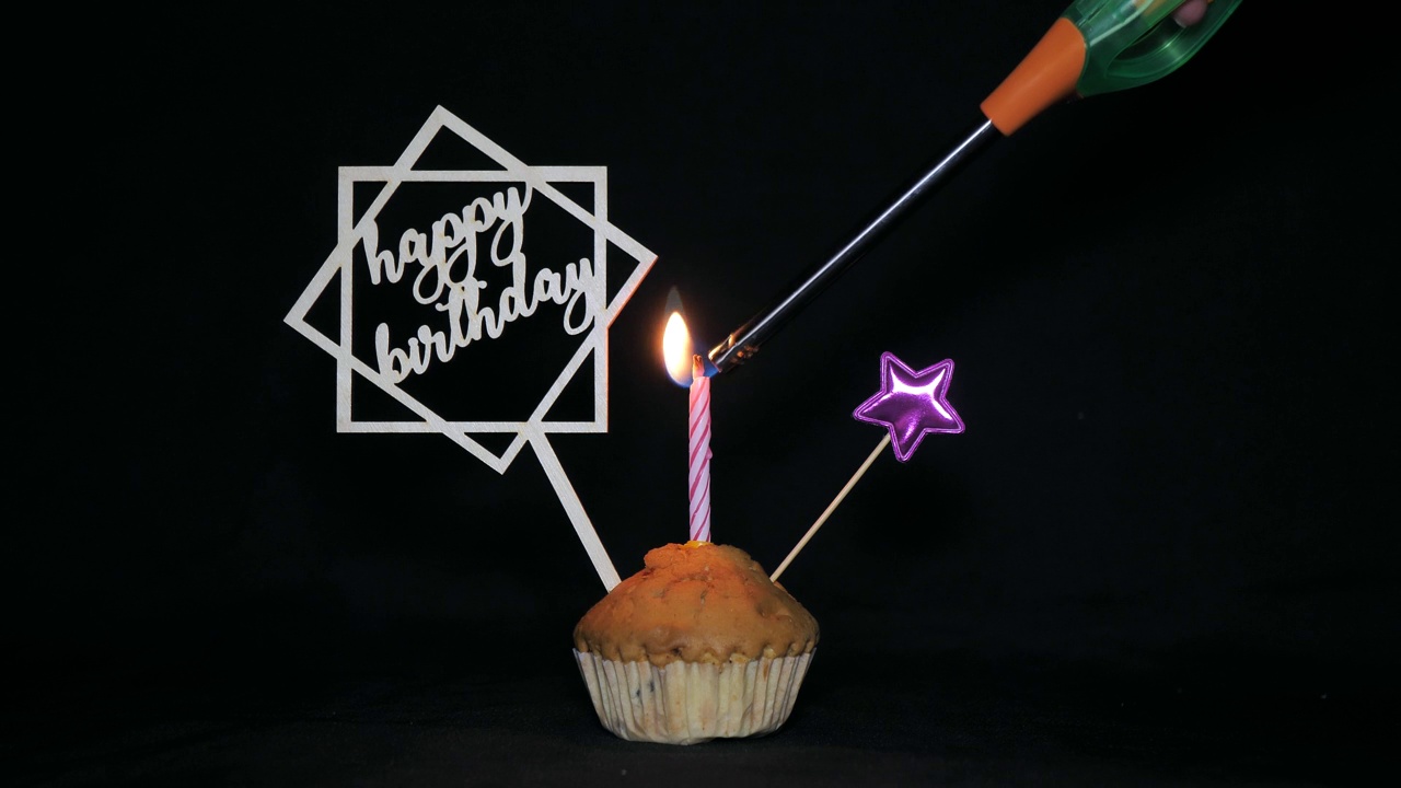 黑色背景上有蜡烛的节日纸杯蛋糕——生日快乐。有彩色装饰和燃烧的蜡烛的纸杯蛋糕。在纸杯蛋糕上点上节日蜡烛视频下载