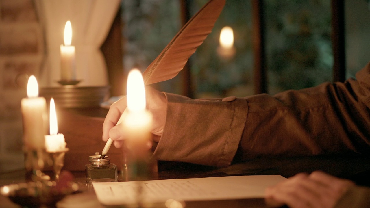 一幅18世纪的场景，由多支蜡烛照亮，一个男人坐在书桌前，拿着墨水瓶和羽毛笔写信。视频素材