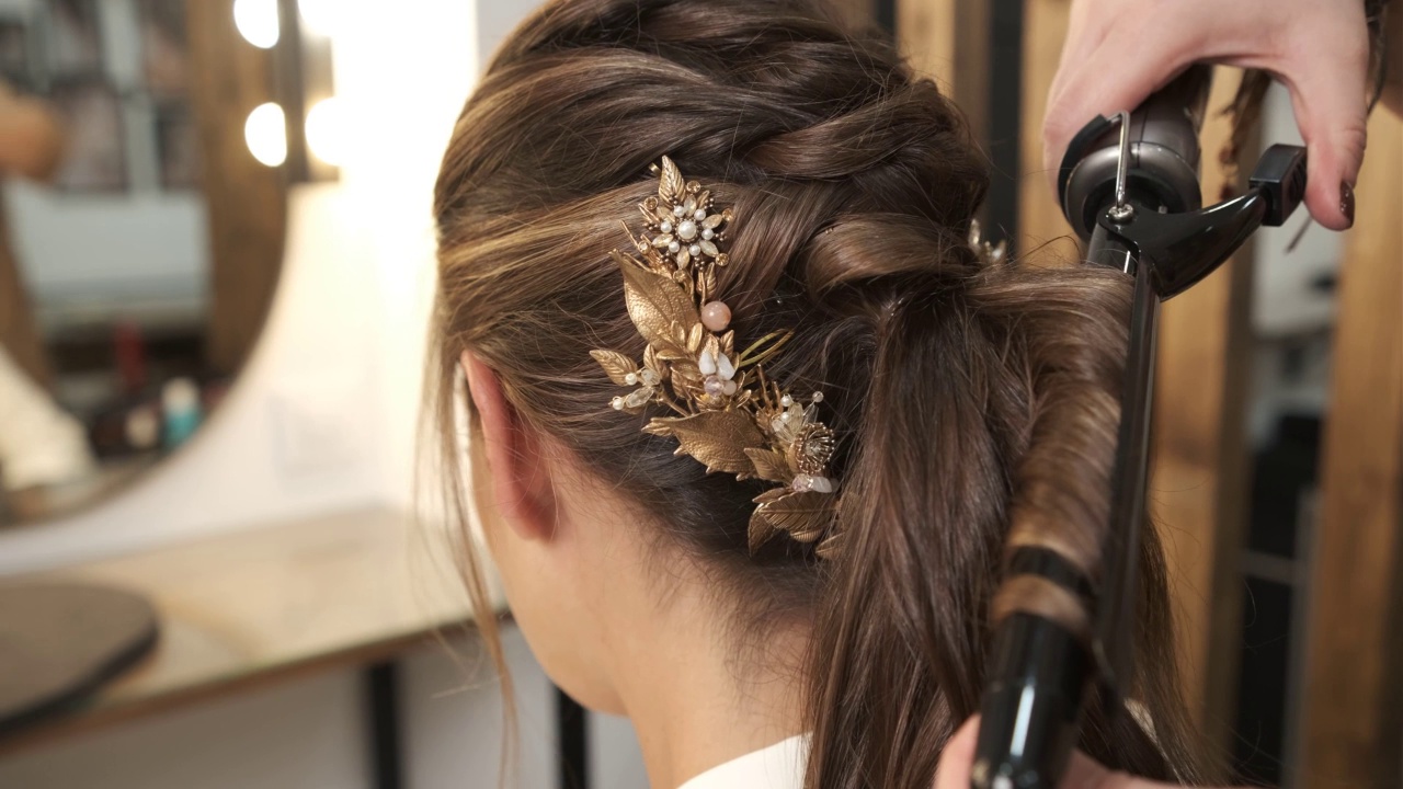 专业的发型师在美容院做她的婚礼发型时卷曲客户的头发。视频下载