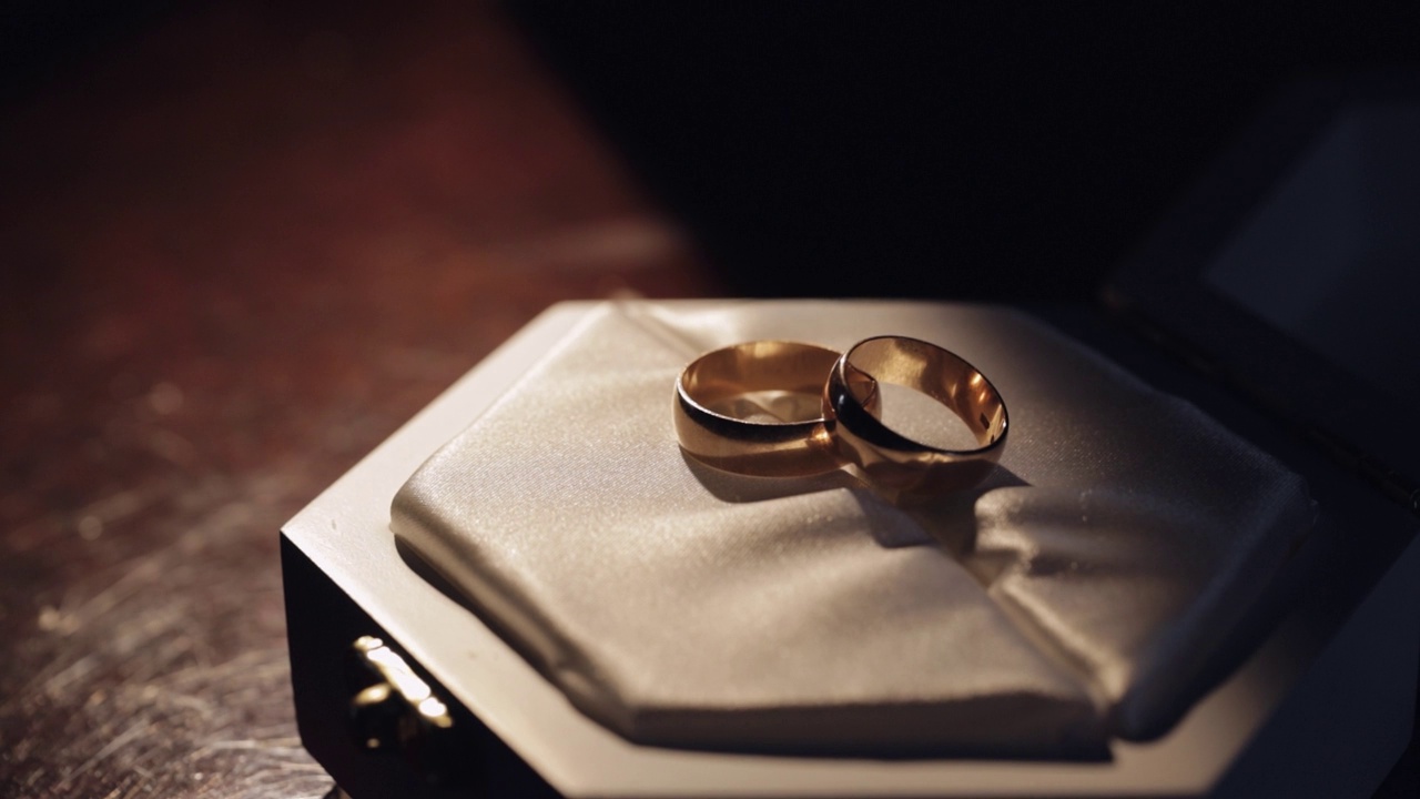 两枚金色的结婚戒指躺在白色的礼品盒上闪耀着温暖的光芒视频素材
