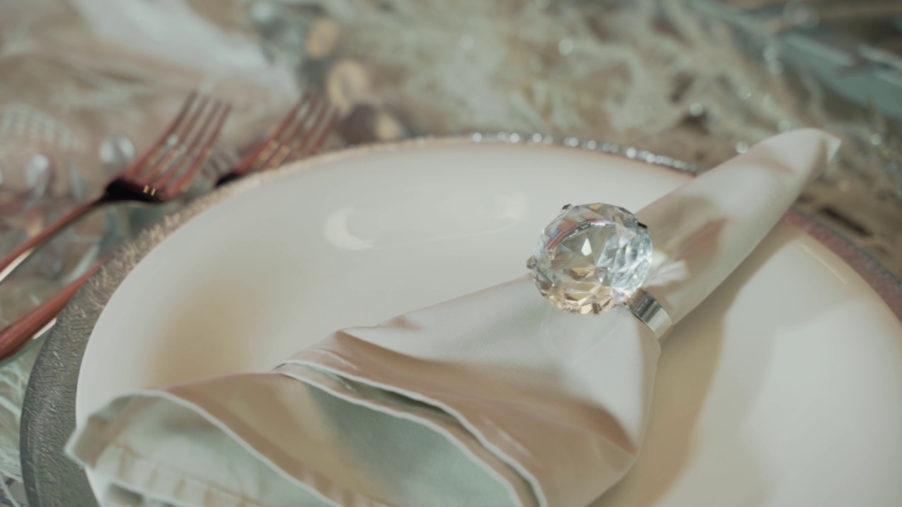 一张餐巾的特写镜头，在美丽的闪光闪光的戒指躺在一个白色的盘子，准备参加婚礼宴会。为新婚夫妇布置漂亮的婚礼餐桌视频下载
