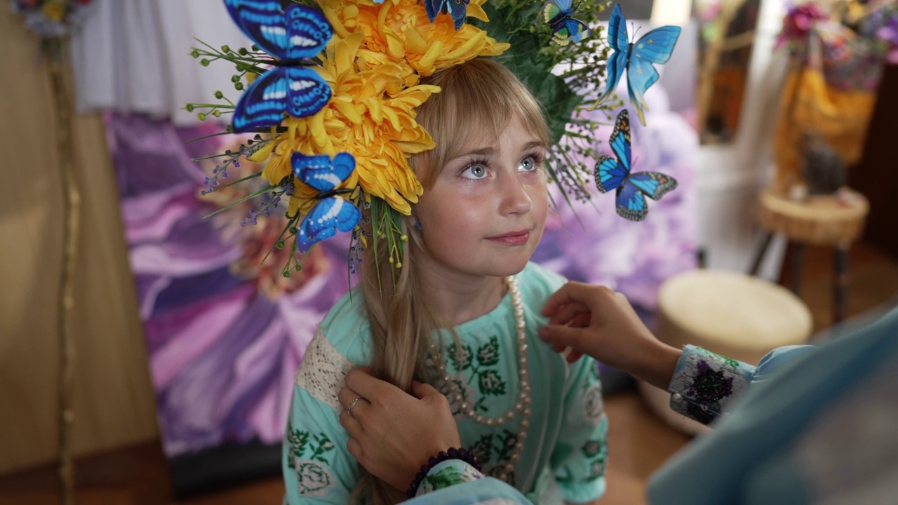 迷人的女孩的肖像头花环和蝴蝶仰望站在室内女性的手爱抚头发在慢动作。可爱的乌克兰女儿对着妈妈微笑。视频素材