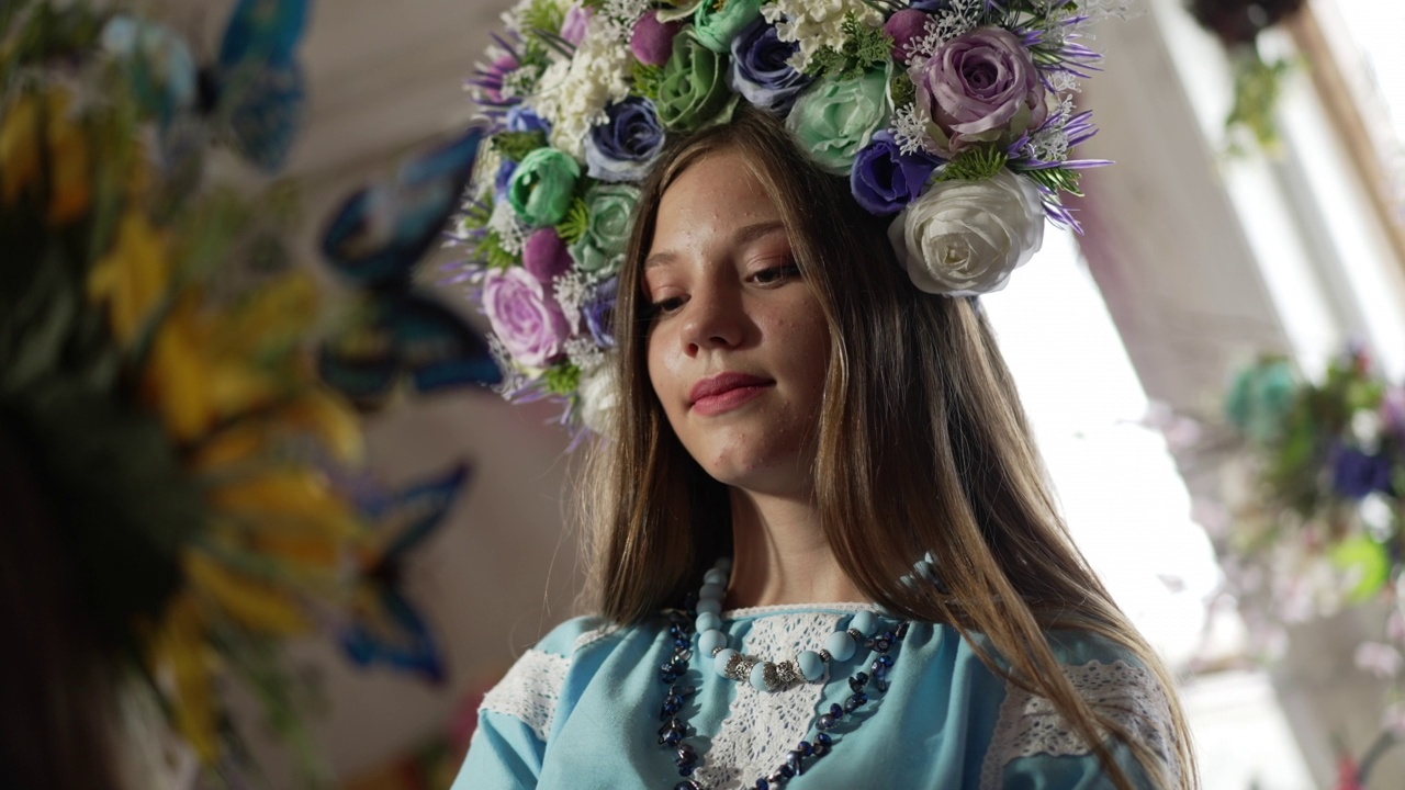 年轻自信的乌克兰妇女穿着刺绣民族服装的肖像，用慢镜头触摸传统的头花环。微笑美丽的女士站在室内看向别处。视频素材