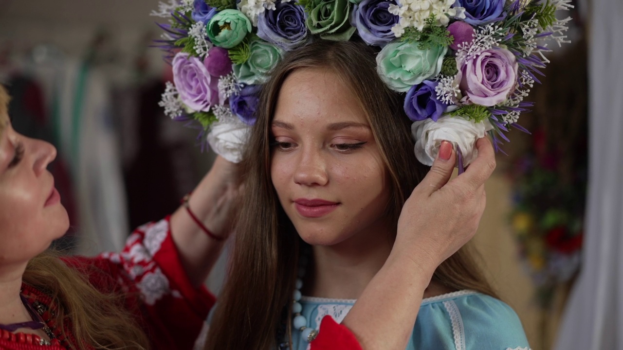 照片中的乌克兰年轻女子面带微笑，站在室内，母亲戴上发圈，头上戴着鲜花。近景苗条华丽的女士在室内民族服装。视频素材