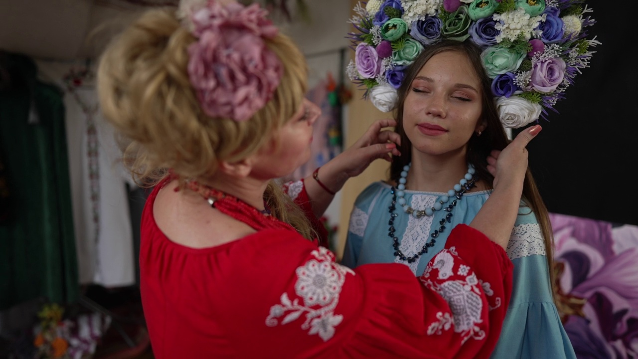 美丽苗条的年轻女子的肖像在乌克兰民族服装站在室内与母亲抚摸头发在慢动作。女儿穿着传统服装，面带微笑，自信满满。视频素材