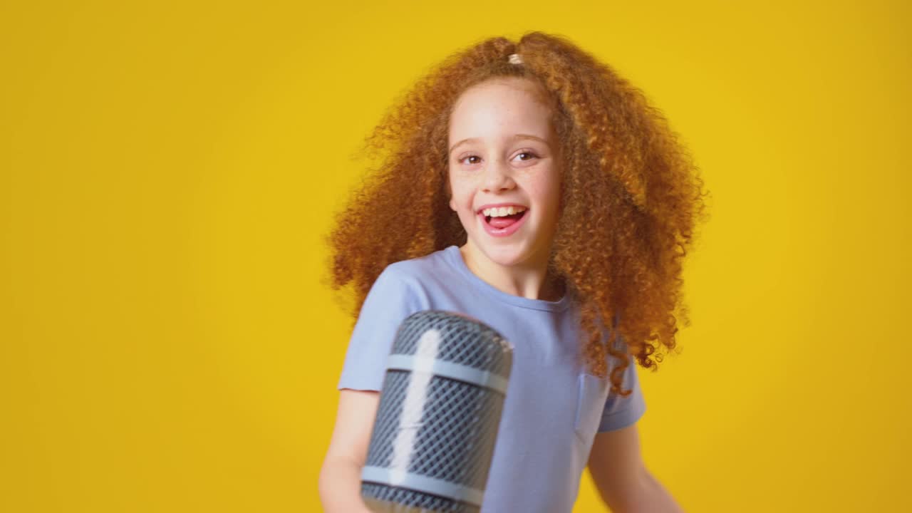 工作室拍摄的女孩唱卡拉ok进入玩具充气麦克风对黄色背景-拍摄的慢动作视频下载