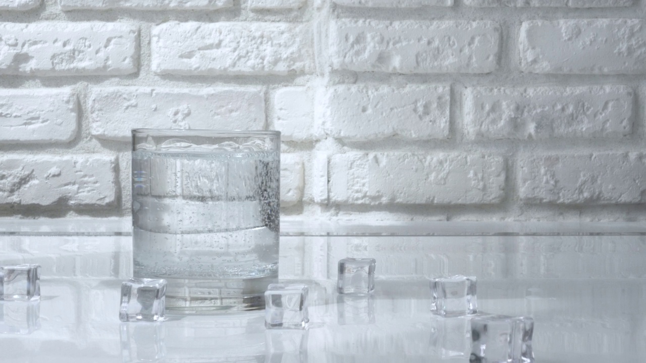 在白砖墙的背景下，向透明玻璃中倒入苏打水。用玻璃杯喝矿泉水视频素材