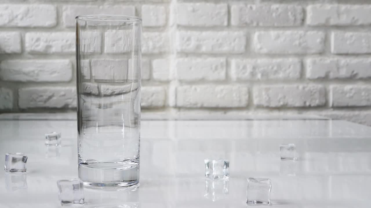 将水倒入一个透明的玻璃杯中，在白色砖墙的背景下喝一杯冷冻矿泉水。水里有气泡视频素材