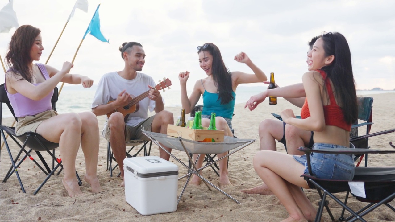 一群亚洲年轻男女在海滩上聚会。迷人的快乐的朋友，旅行者唱歌和跳舞，在海边露营，享受假期，在热带海岛度假旅行视频素材