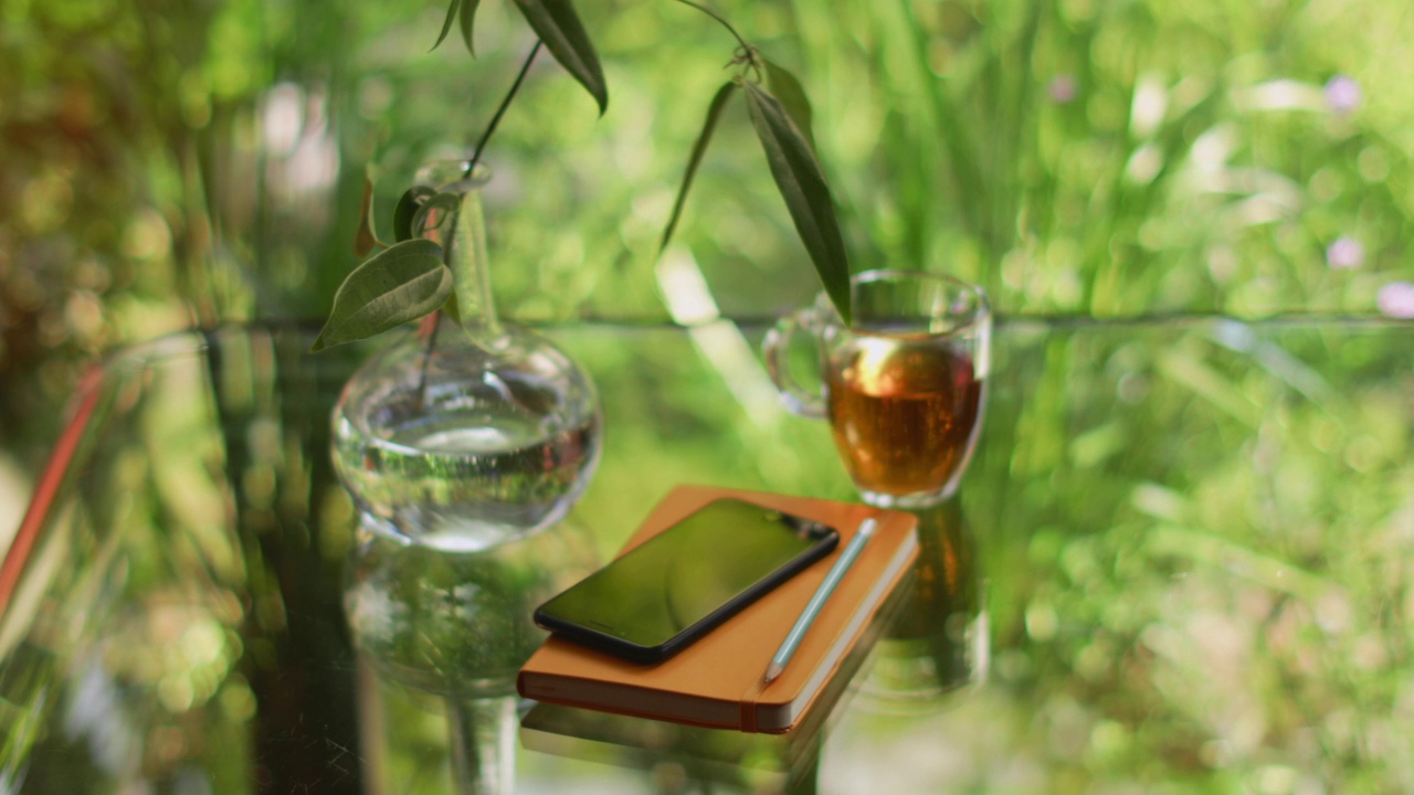 茶和花瓶在反光的桌子上，日记和智能手机视频素材