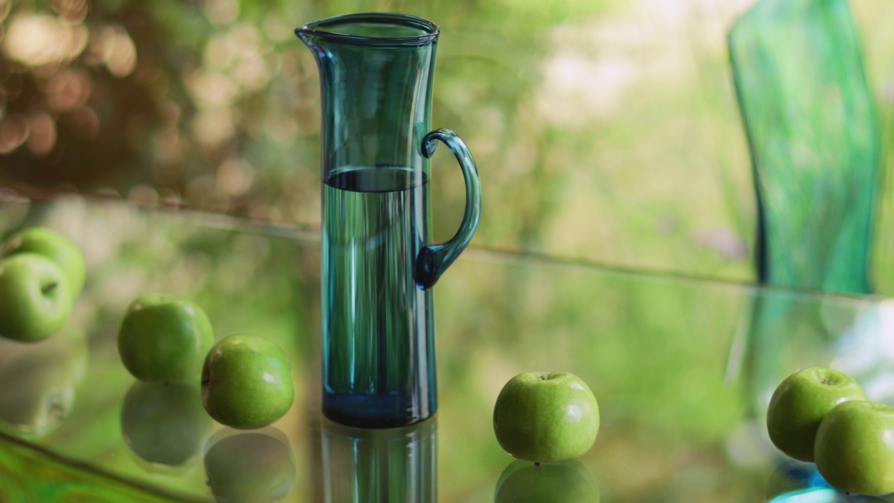 绿苹果和高大的玻璃水罐在玻璃桌子上视频素材