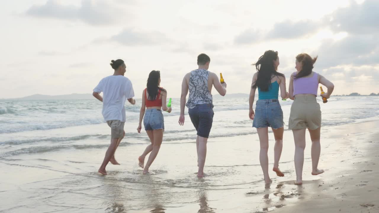 一群亚洲年轻男女朋友一起在海滩上散步。迷人的旅行者感到快乐和放松，在热带海岛度假旅行时喝着一瓶啤酒视频素材