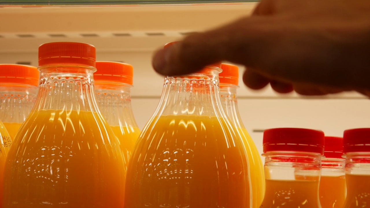 冰箱里许多橙汁瓶子的特写，一个男人的手拿着一个视频素材