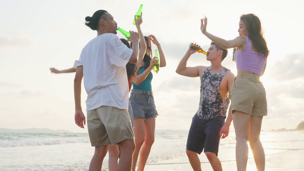 一群亚洲年轻男女朋友一起在海滩上散步。迷人的旅行者感到快乐和放松，在热带海岛度假旅行时喝着一瓶啤酒视频素材