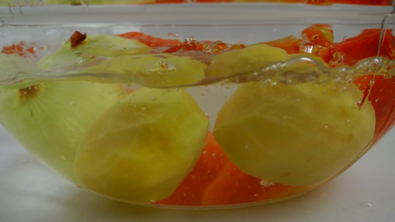 落在一碗水里的蔬菜洋葱，土豆和胡萝卜。缓慢的运动。视频素材