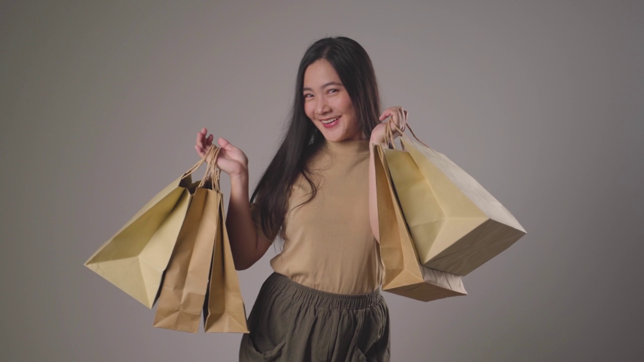 自信的亞洲女人開心地拿著購物袋跳舞微笑著看著鏡頭。4 k的視頻。視頻下載