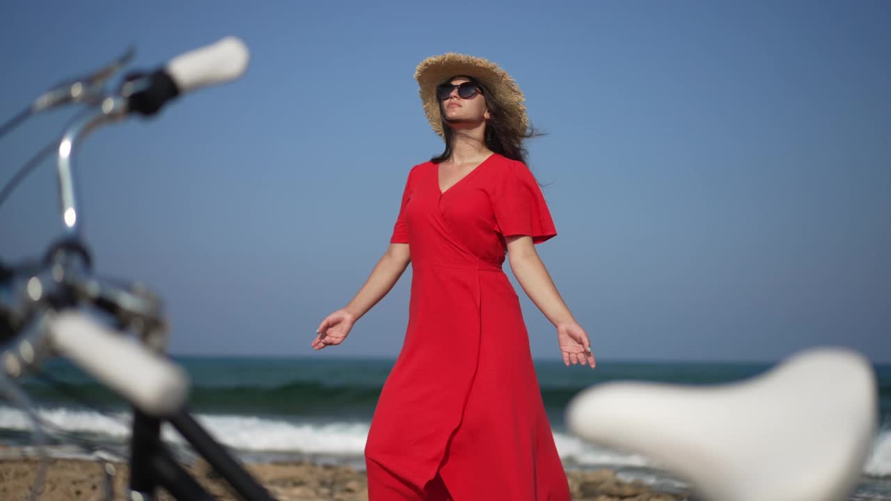 美丽自信的年轻女子的肖像在慢动作中举起手，站在阳光明媚的塞浦路斯地中海的背景。愉快轻松的白人游客享受休闲与自行车。视频素材