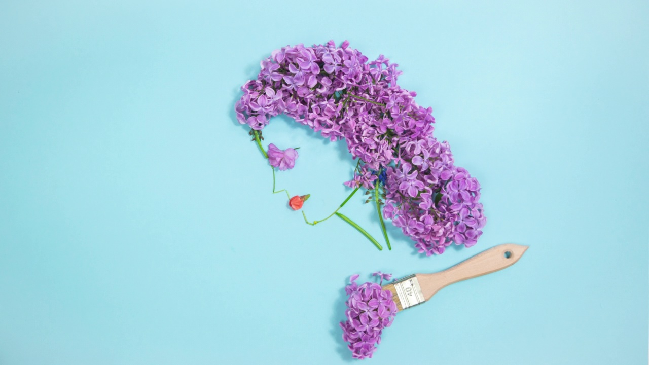 这支画笔用自然的花朵、细枝和紫丁香画出了一个年轻女子的侧面肖像。浅蓝色背景与复制空间。视频下载