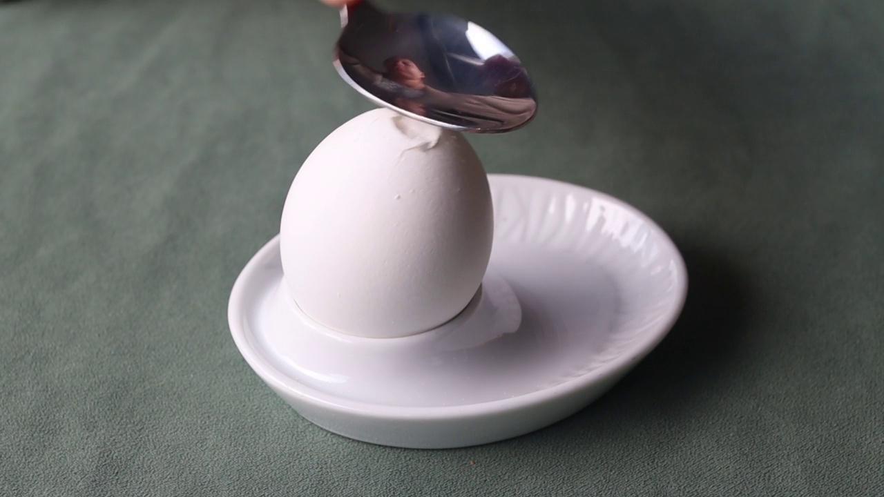 用勺子在蛋架上敲开一个煮熟的鸡蛋。视频下载