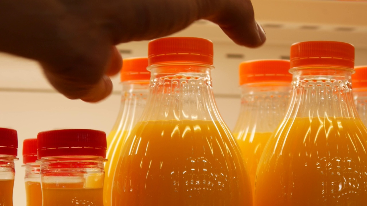 冰箱架子上有很多橙汁瓶子，一个男人拿走了一个视频素材