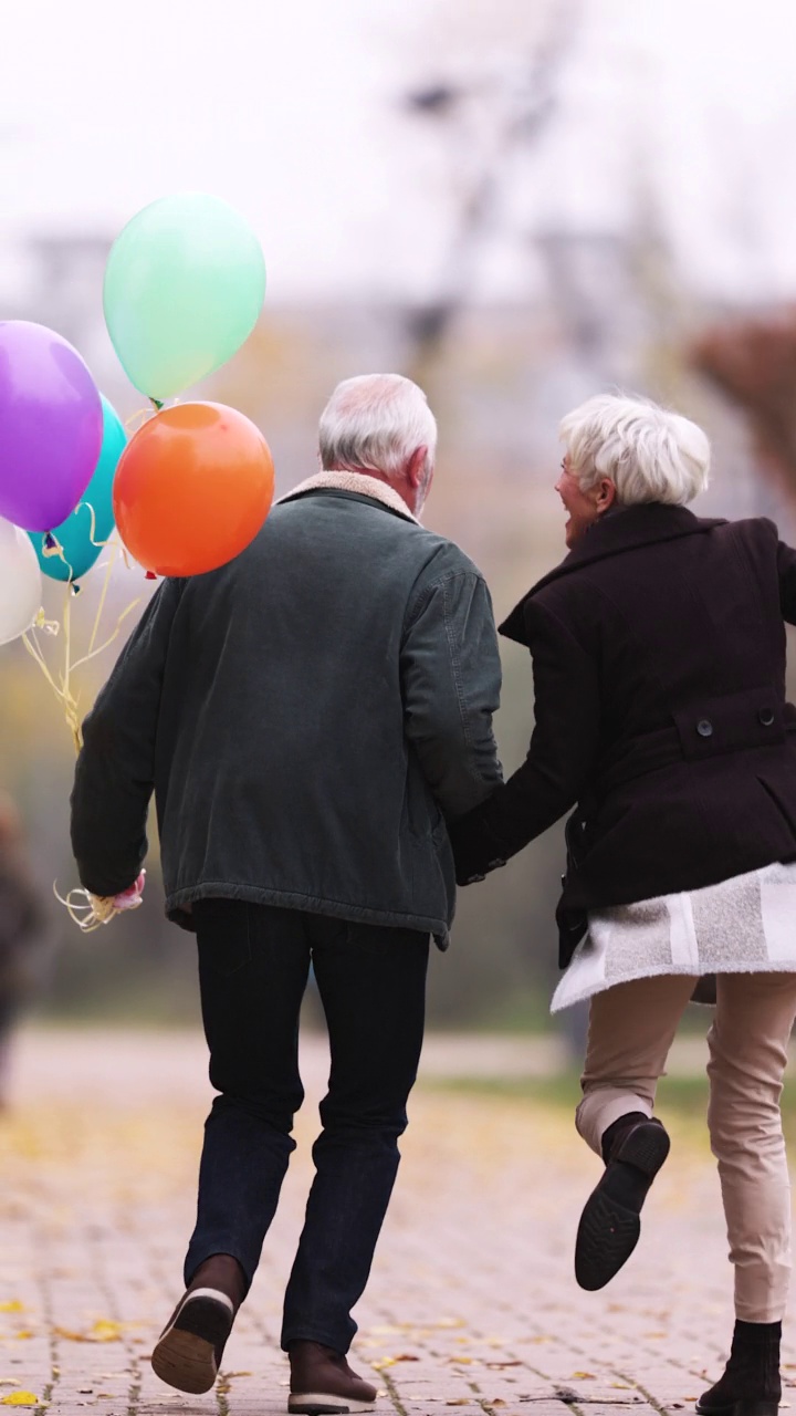 无忧无虑的老夫妇在公园里拿着气球奔跑的垂直视频视频素材