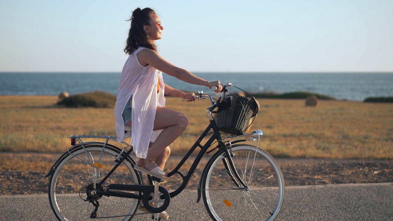 兴奋的年轻美丽的自行车手举起手骑自行车在塞浦路斯风景的背景慢动作。侧视图跟踪拍摄快乐的高加索妇女享受假期户外自行车。视频素材