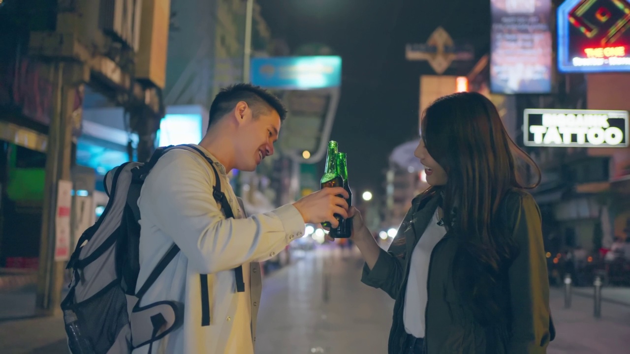 亚洲有吸引力的夫妇一起喝酒和聚会。年轻的男人和女人在城市旅游，在假期度假一起拿着啤酒在黑暗的夜晚在路上。视频素材