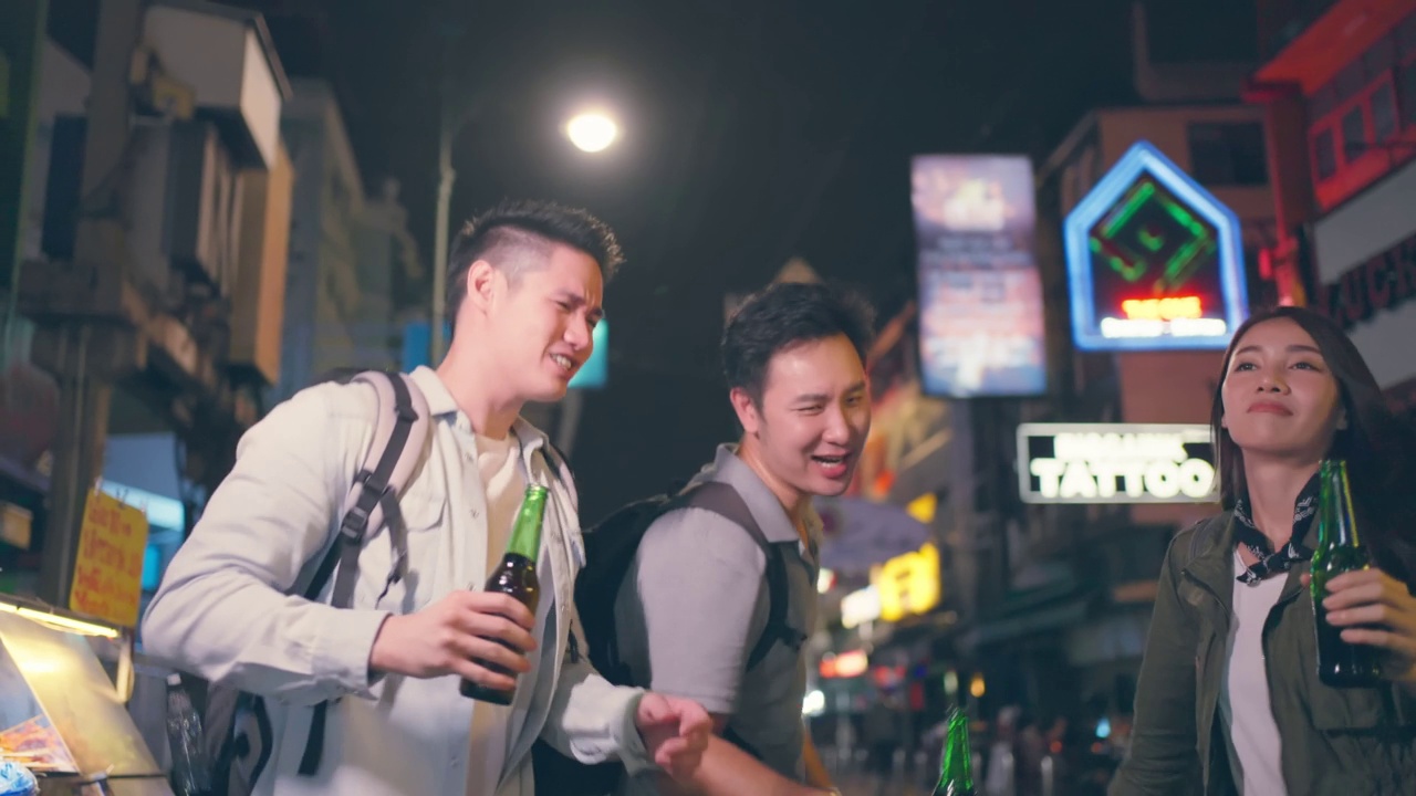 一群亚洲人在一起喝酒、喝酒、开派对。年轻的男人和女人在城市旅游旅游，在假期一起在黑暗的夜晚拿着啤酒在路上。视频素材