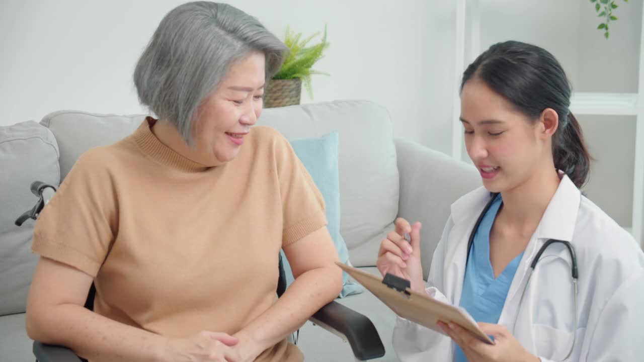 亚裔女医生就诊时面带微笑填写老年病人体检表，将数据写入文件夹板，病史，疾病预防，亚裔老年妇女体检。视频下载
