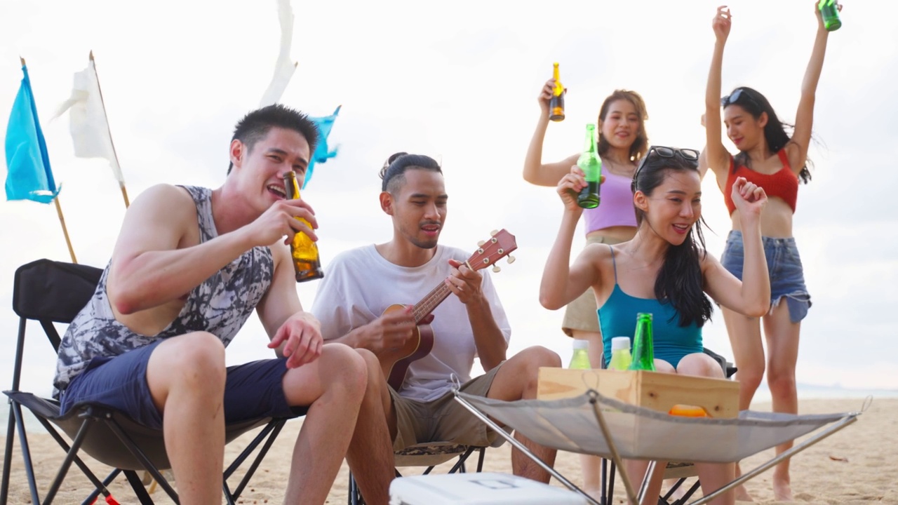 一群亚洲年轻男女在海滩上聚会。吸引快乐的朋友，在海边露营，唱歌，跳舞，享受假期，在热带海岛度假旅行视频素材