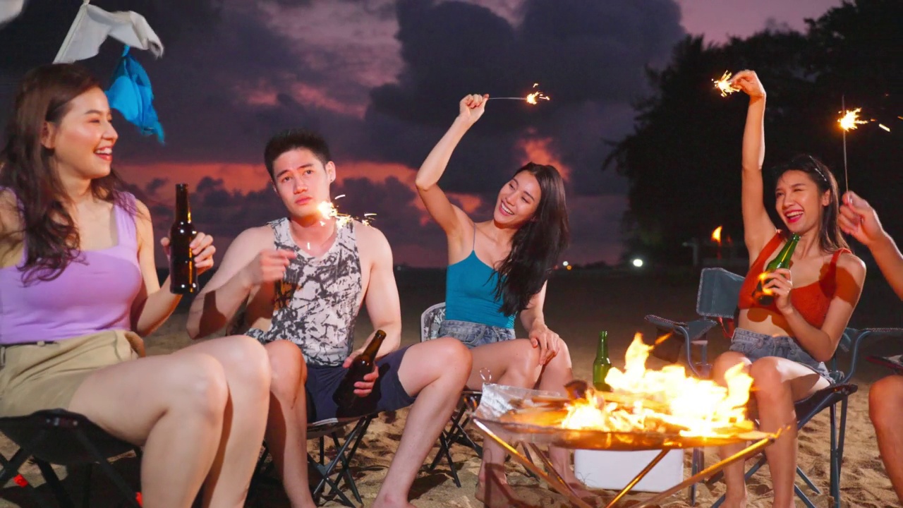 一群亚洲年轻男女晚上在海滩上聚会。迷人的朋友们在海边露营时唱歌跳舞，一起在热带海岛度假度假视频素材