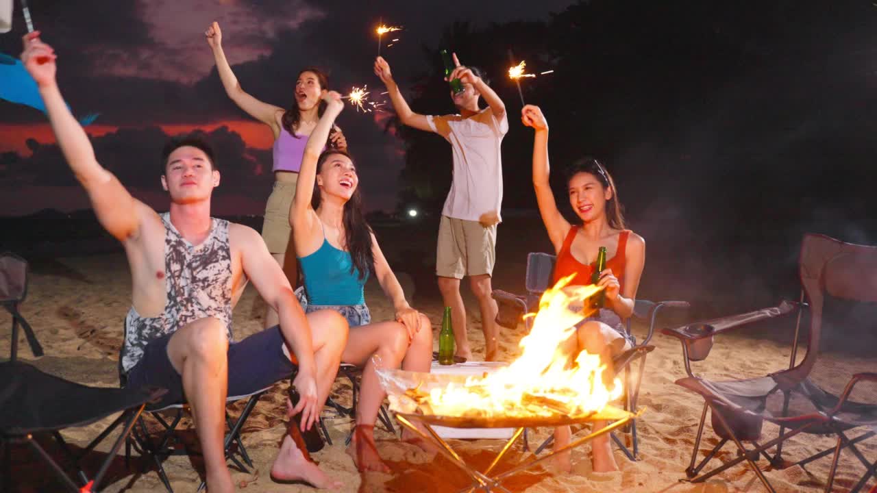 一群亚洲年轻男女晚上在海滩上聚会。迷人的朋友们在海边露营时唱歌跳舞，一起在热带海岛度假度假视频下载