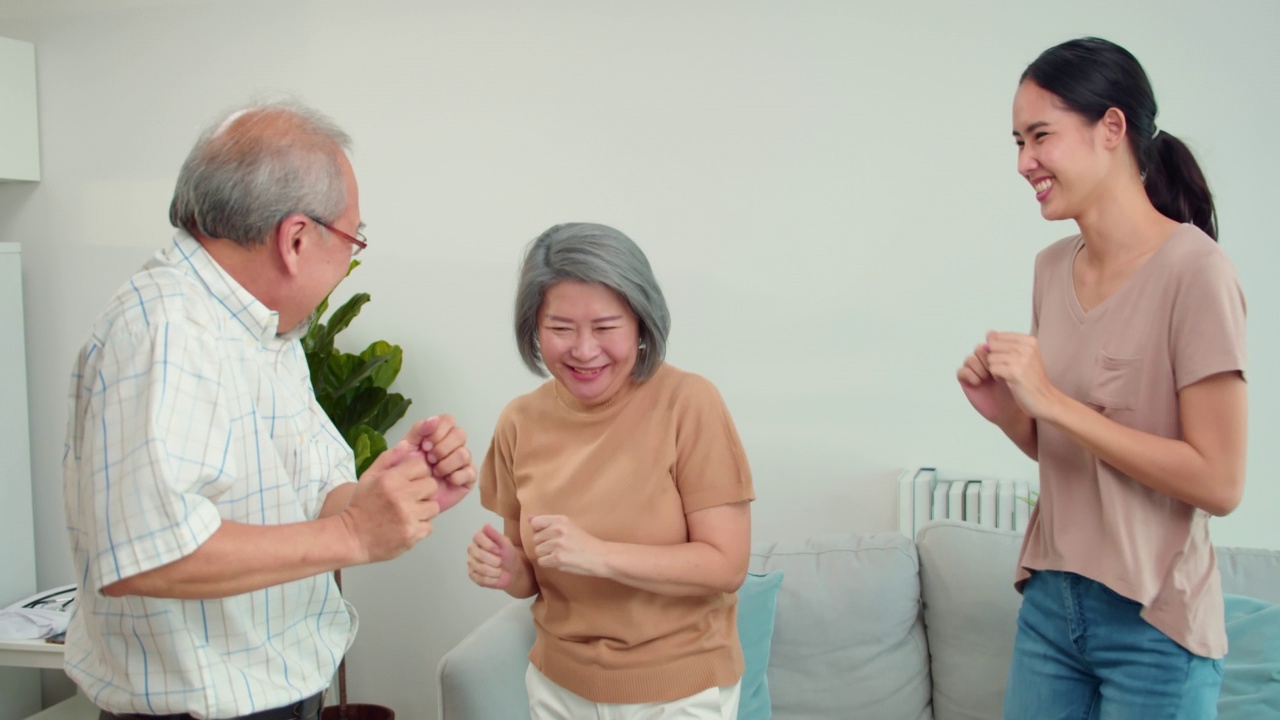亚洲年迈的父母和现代的女儿在家里的客厅里一起玩耍。女儿们和父母们一起跳现代舞，一起感受节日的快乐。家庭的概念。视频下载