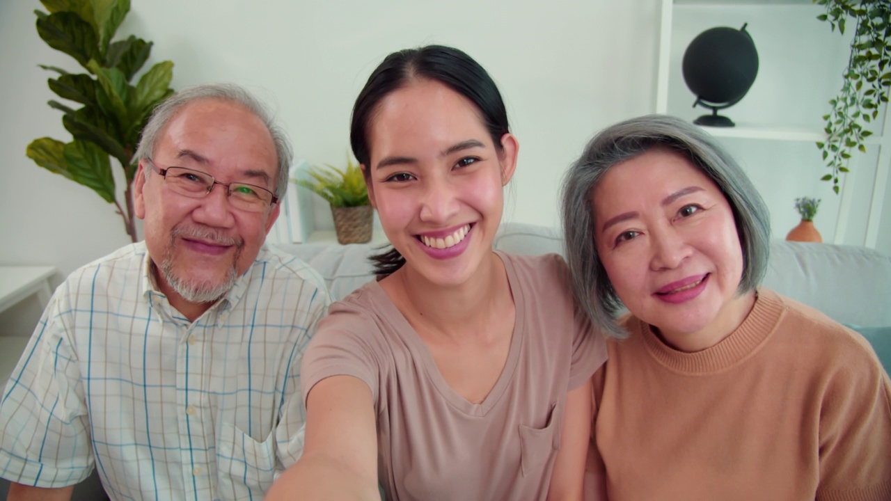 前视图的老人家庭的亚洲父母和女儿是快乐的，笑着谈论通过他们的智能手机视频通话。十几岁的女儿拿着手机，她的父母正在向她打招呼。视频下载