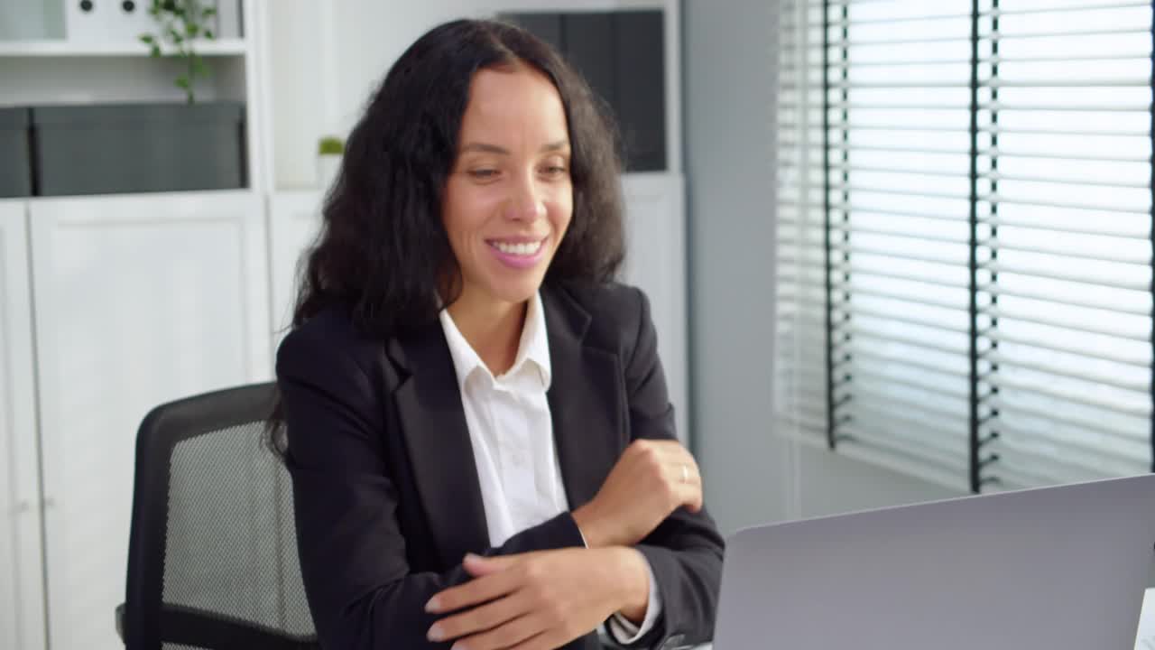 美丽年轻的拉丁女商人在家庭办公室工作地点的笔记本电脑视频通话。与客户或同事聊天时微笑着挥手问候对方的女性。经营理念。视频下载