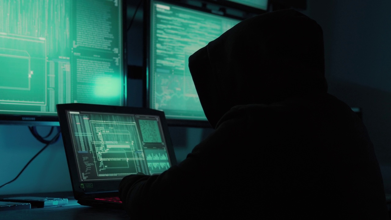 一名黑客程序员穿着连帽衫，戴着黑色黑客面具，隐藏自己的身份，利用电脑进行黑客活动。这就是黑暗网络的概念视频素材