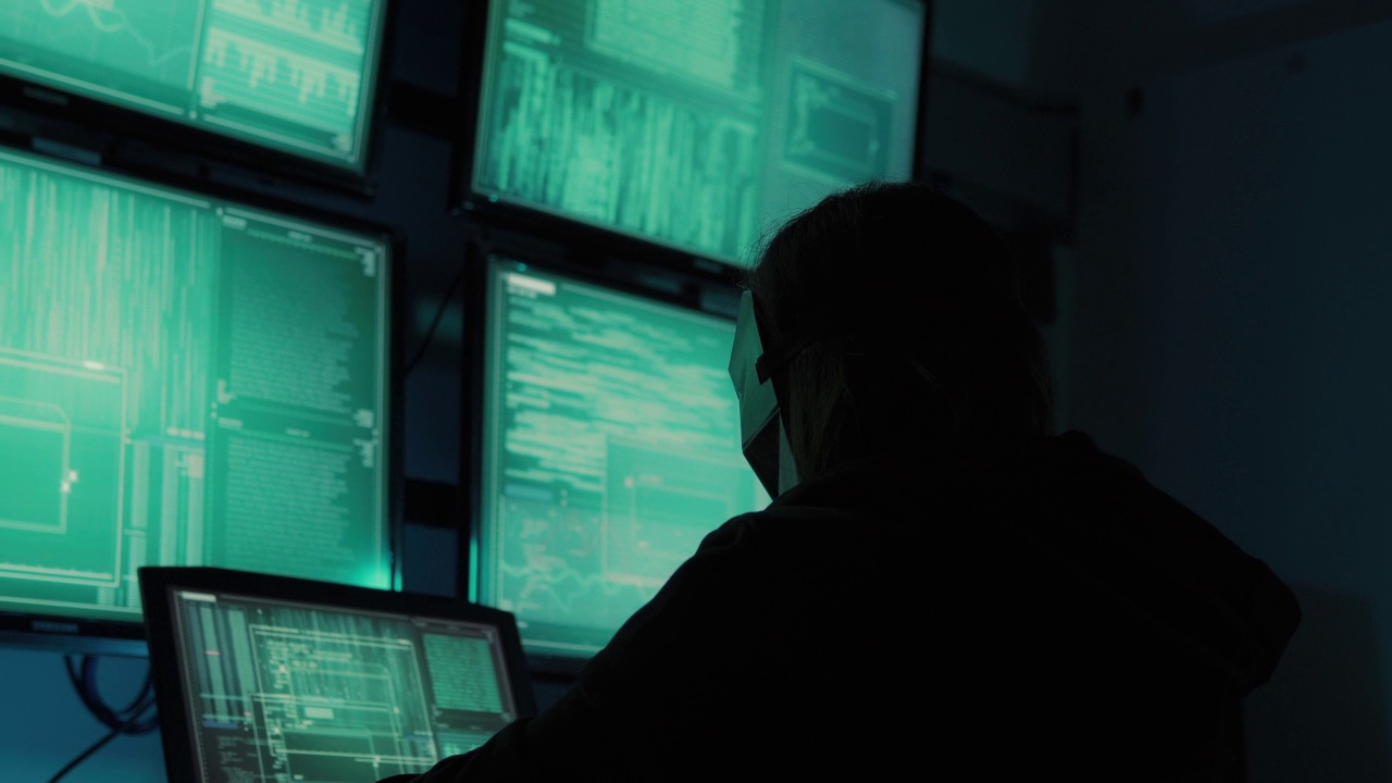 一名黑客程序员穿着连帽衫，戴着黑色黑客面具，隐藏自己的身份，利用电脑进行黑客活动。这就是黑暗网络的概念视频素材