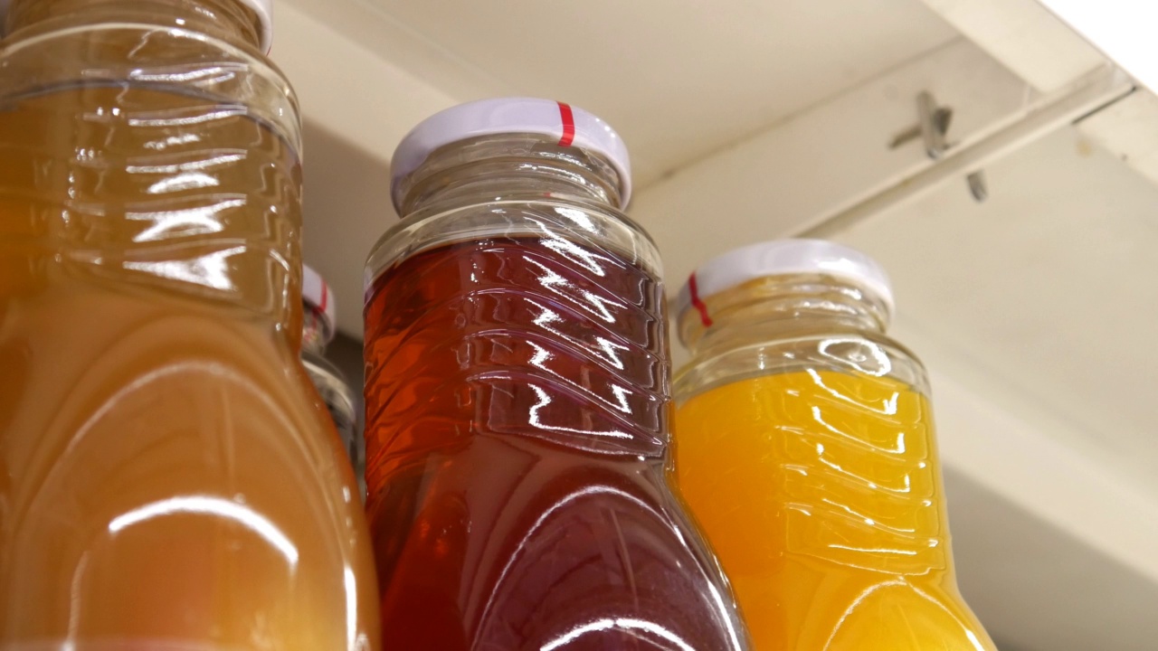 商店货架上许多装着各种果汁的漂亮玻璃瓶的特写，买家的手拿着一个视频素材