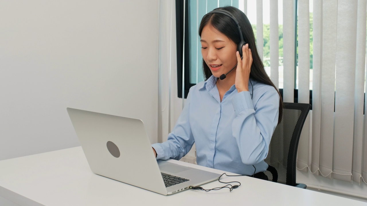 年轻的女商人在办公室的办公桌上戴着耳机讲电话视频素材